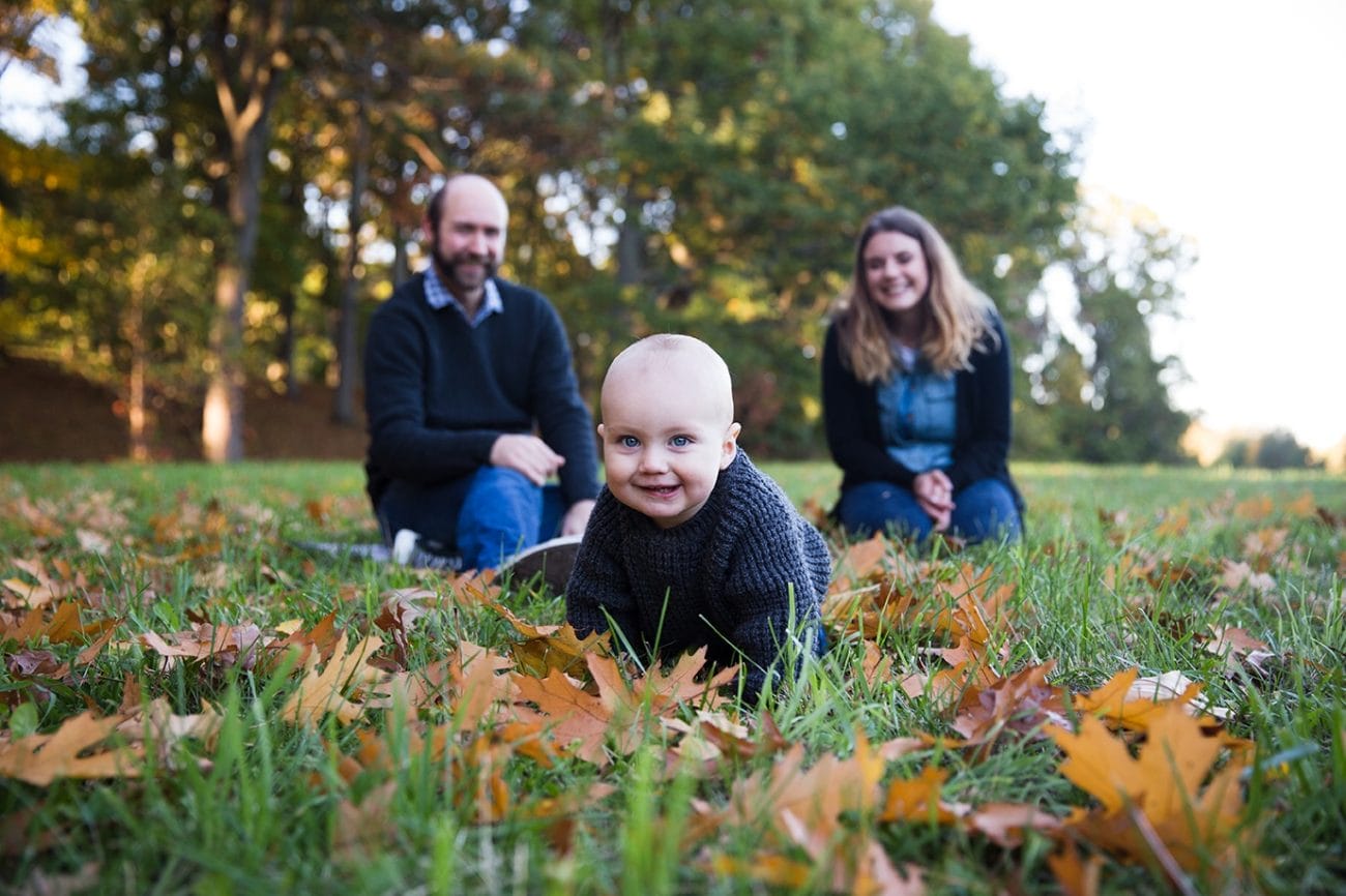 A lifestyle photograph of a baby crawling in the Arnold Arboretum during a fall family session in Boston, Massachusetts