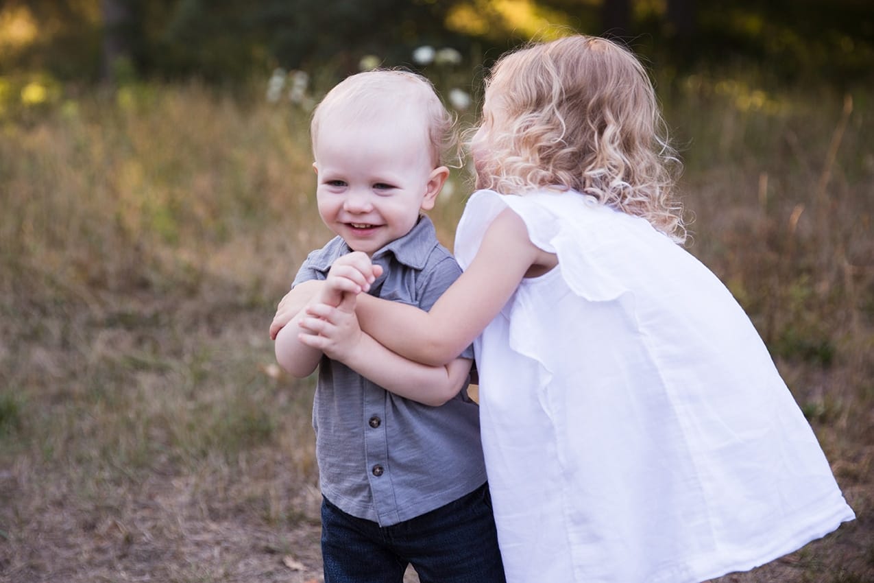 A documentary photograph of a little girl hugging her little brother during their Arnold Arboretum Family Session in Boston, Massachusetts