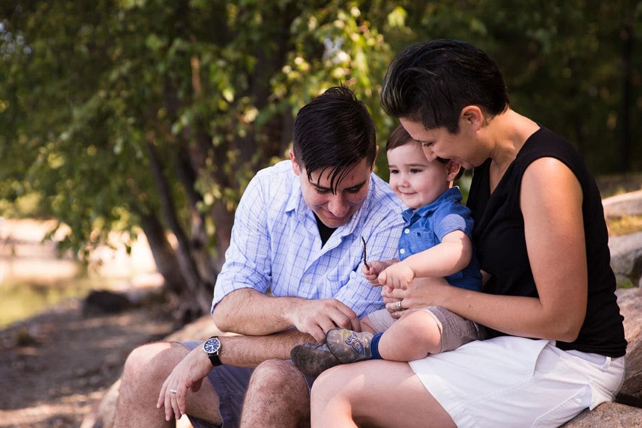 A lifestyle portrait of a family sitting together on rocks at Jamaica Pond during their family session in Boston, Massachusetts