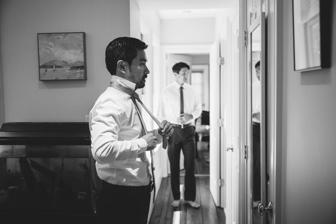 A documentary photograph of a groom tying his tie at home before his artists for humanity wedding in Boston, Massachusetts