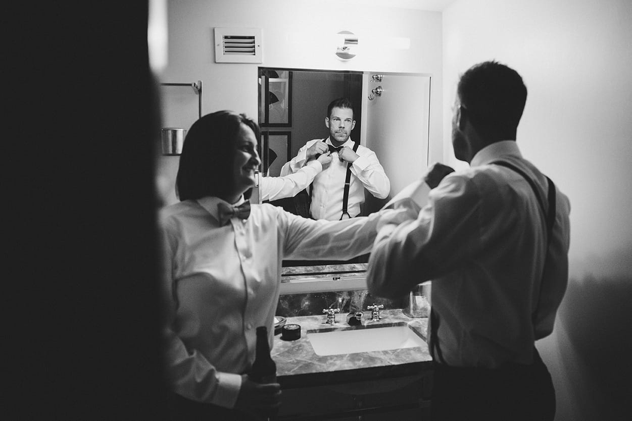 A documentary photograph of a friend helping the groom with his bowtie before his old south meeting house and marliave wedding in Boston, Massachusetts