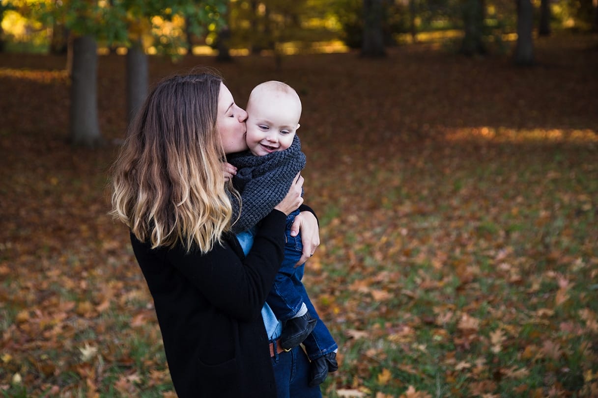 A documentary photograph of a mom kissing her baby boy during their lifestyle family photo session in the Arnold Arboretum