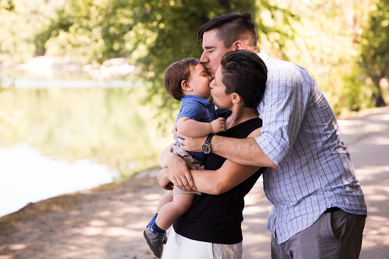 A lifestyle portrait of parents kissing their baby boy during a Jamaica Pond family session