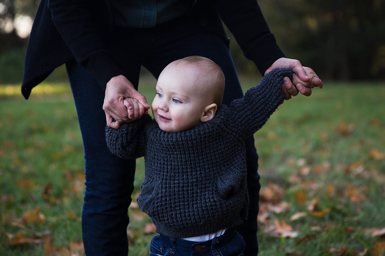 A lifestyle portrait of a baby learning to walk during an Arboretum Family Session in Boston, Massachusetts