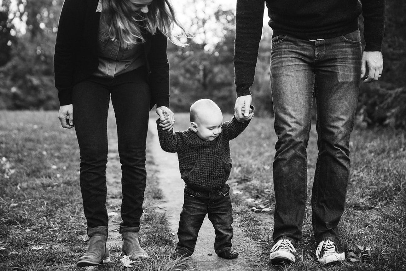 A documentary photograph of a mom and dad holding their babies hands while walking during their Arboretum Family Session in Boston, Massachusetts