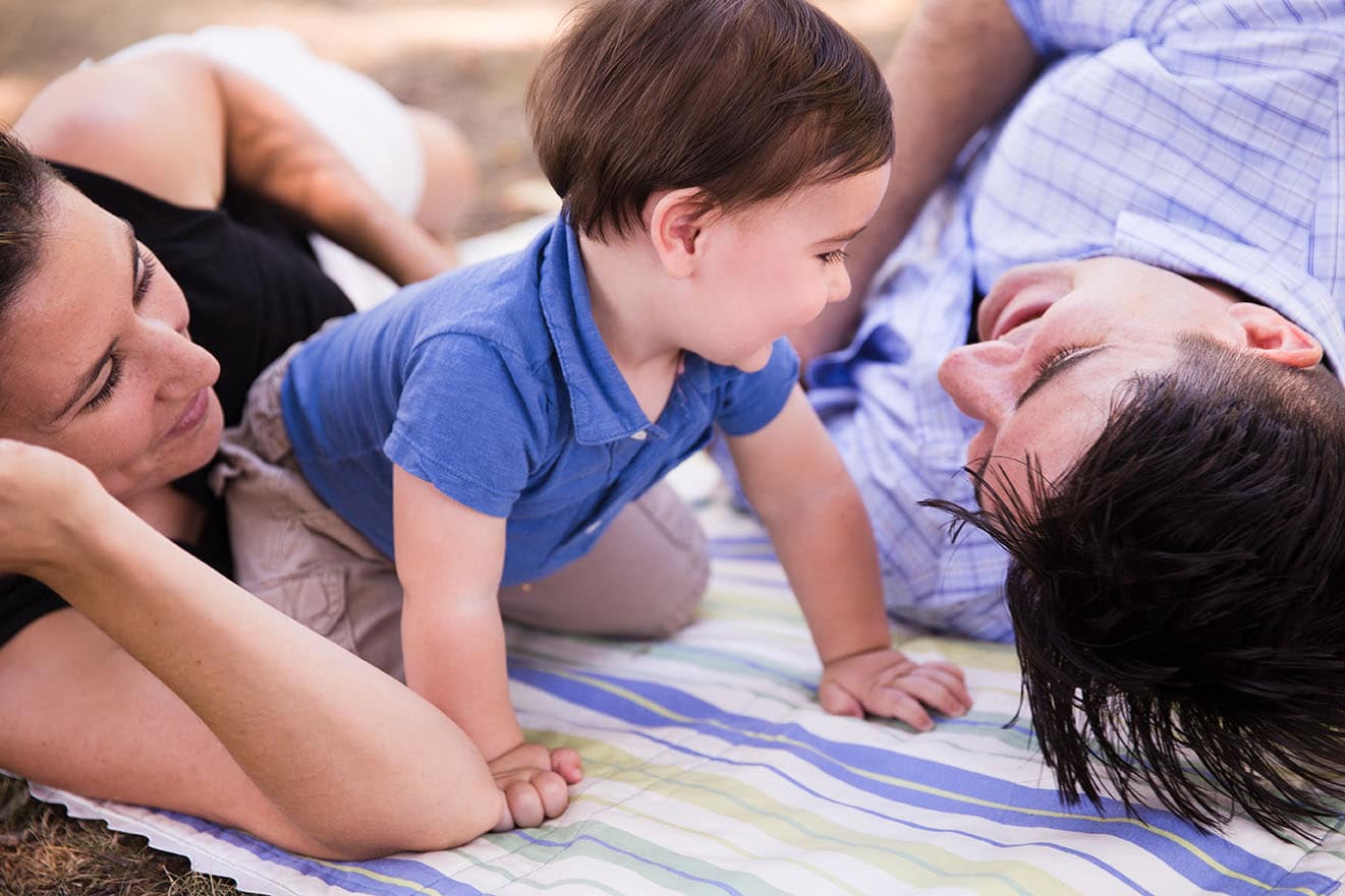 A documentary photograph of a family laying on a blanket during their Jamaica Pond family session in Boston, Massachusetts