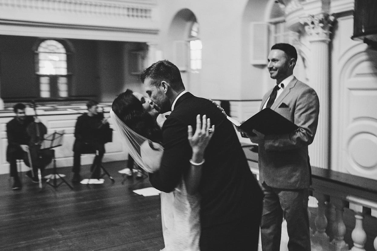 A documentary photograph of a bride and groom kissing during their wedding ceremony at old south meeting house in Boston, Massachusetts