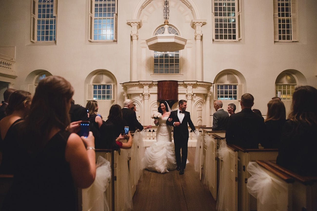 A documentary photograph of a bride and groom walking down the aisle after their wedding ceremony at the Old South Meeting House in Boston, Massachusetts