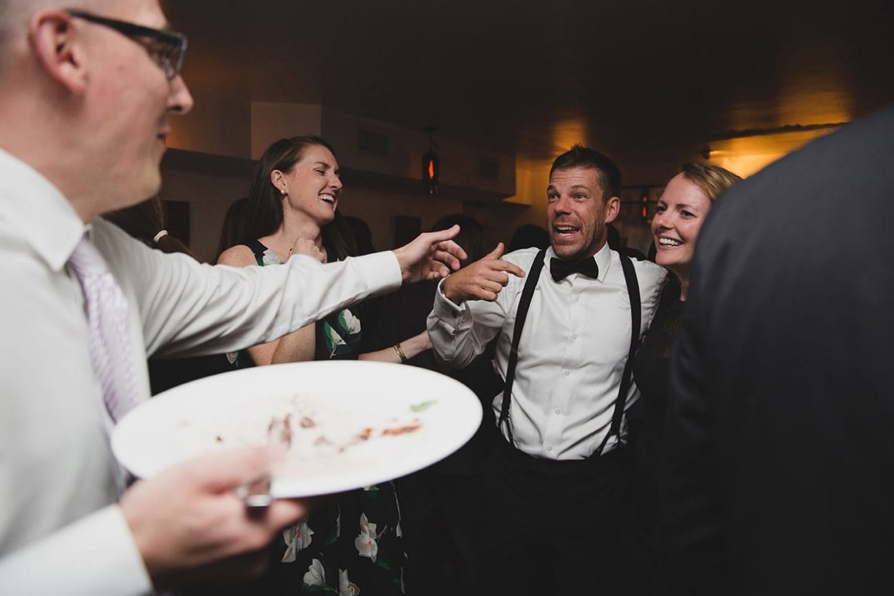 A documentary photograph of guests laughing with the groom during a marliave wedding reception in Boston, Massachusetts