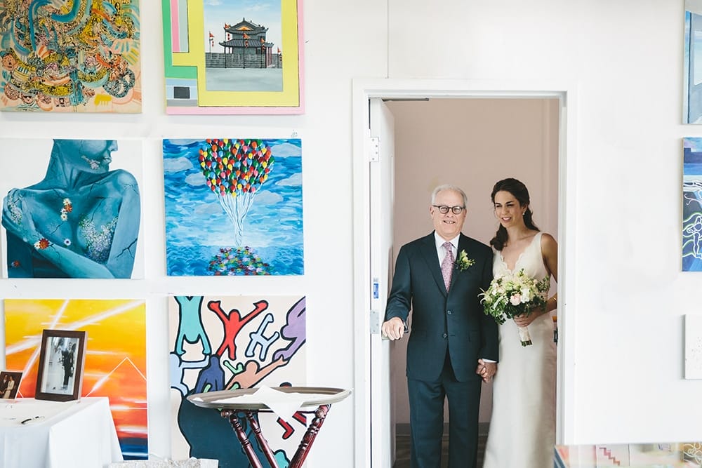 A documentary photograph of a bride holding her father's hand before they walk down the aisle at her Artists For Humanity Wedding in Boston