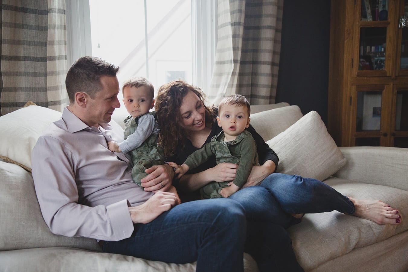 A lifestyle portrait of twin boys sitting on the couch with their parents during an in home family session in Jamaica Plain