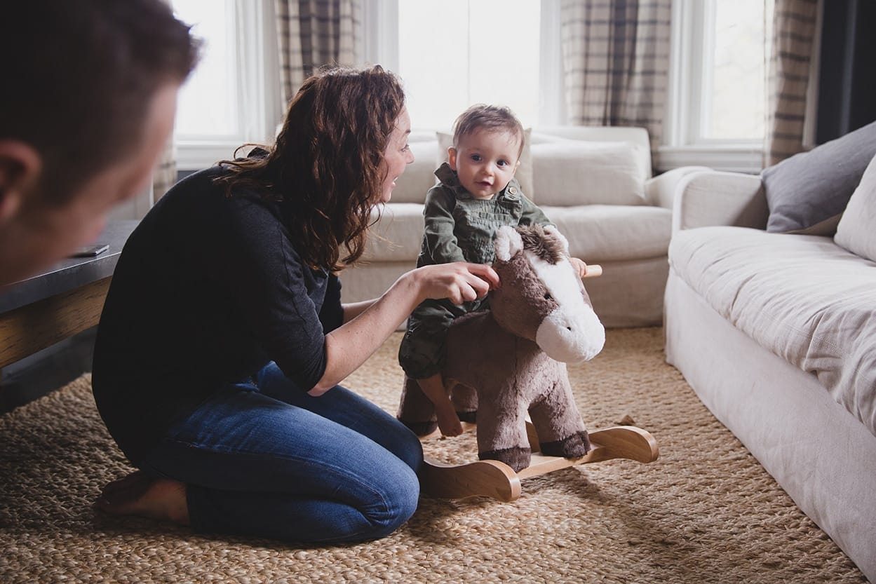 A documentary photograph of a mom helping her son ride his rocking horse during an in home family session in Jamaica Plain