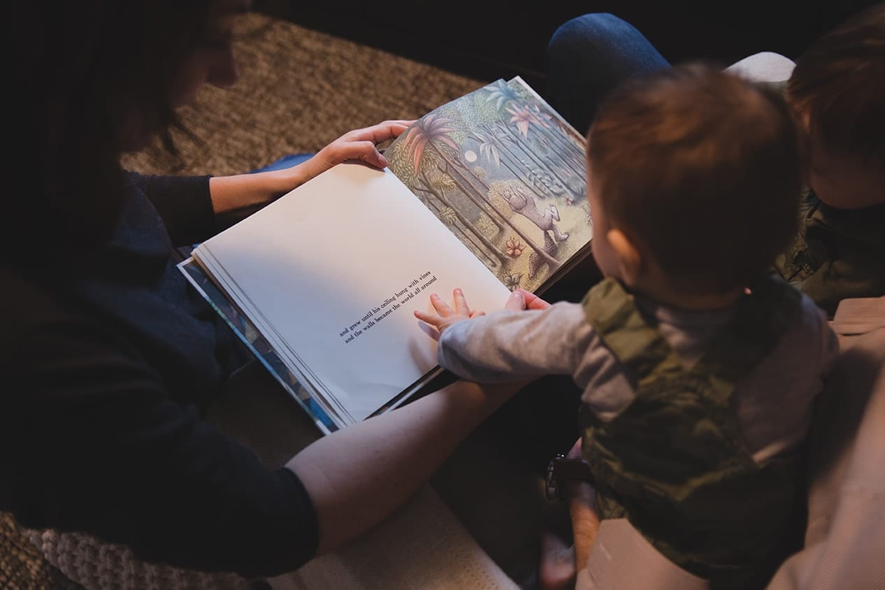 A documentary photograph of a mom reading 'where the wild things are' to her baby boy