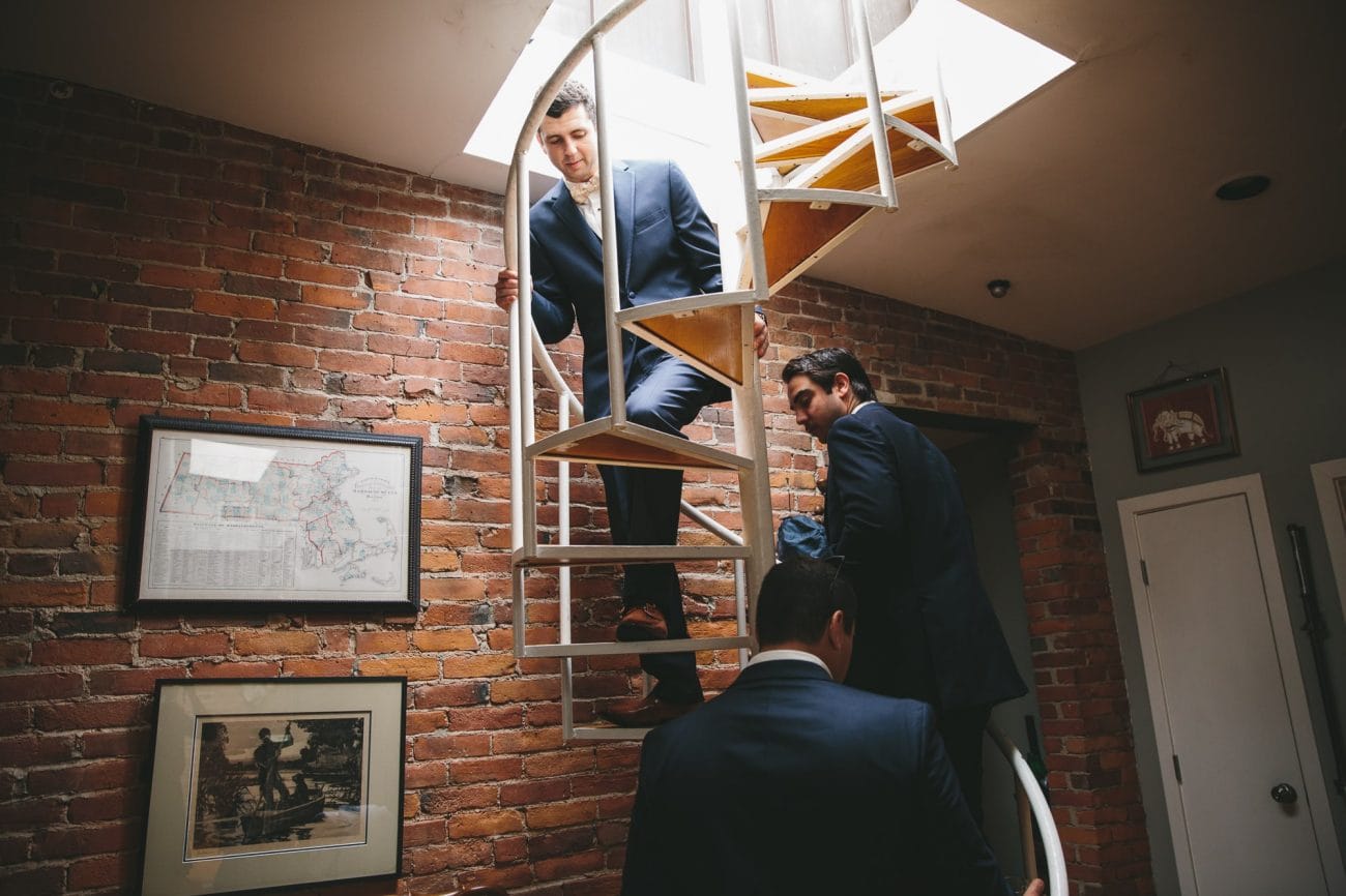 A documentary photograph of groomsmen walking up a spiral staircase before a State Room Wedding in Boston, Massachusetts