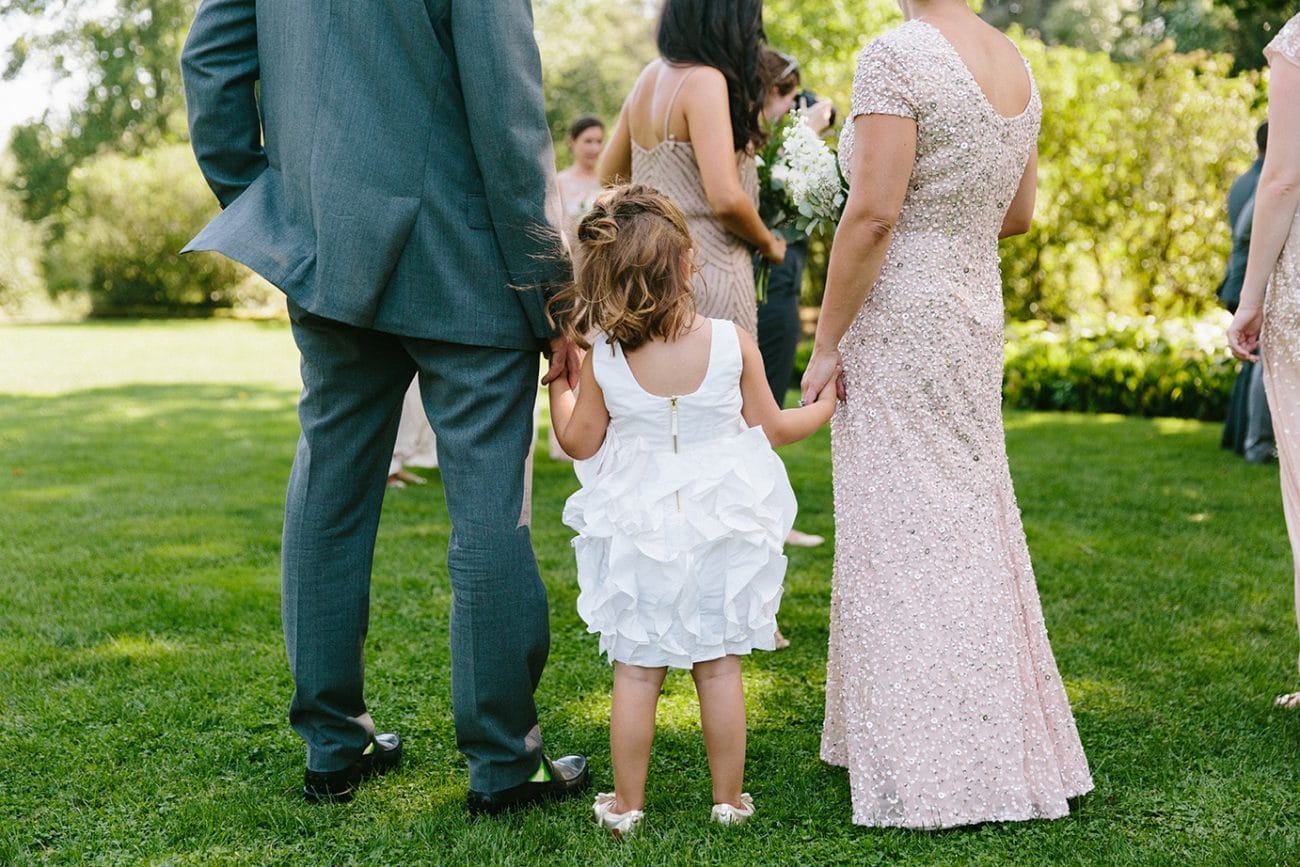 A documentary photograph of a flower girl holding her parent's hands during a Moraine Farm wedding in Beverly, Massachusetts