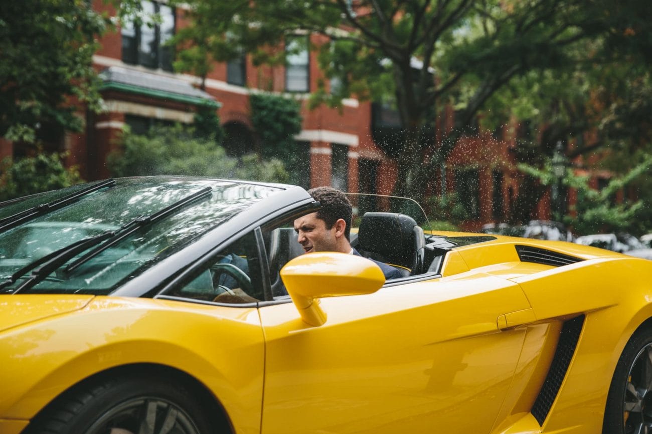 A documentary photograph of a groom accidentally turning on the windshield wipers and spray of a rented lamberghini before his State Room Wedding in Boston, Massachusetts