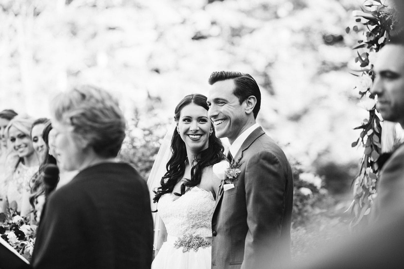 A documentary photograph of a bride and groom smiling during their wedding ceremony at Harrington Farm in Princeton, Massachusetts