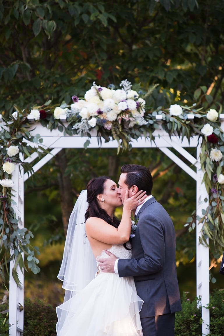 A documentary photograph of a bride and groom sharing their first kiss as husband and wife during their outdoor ceremony at Harrington Farm in Princeton, Massachusetts