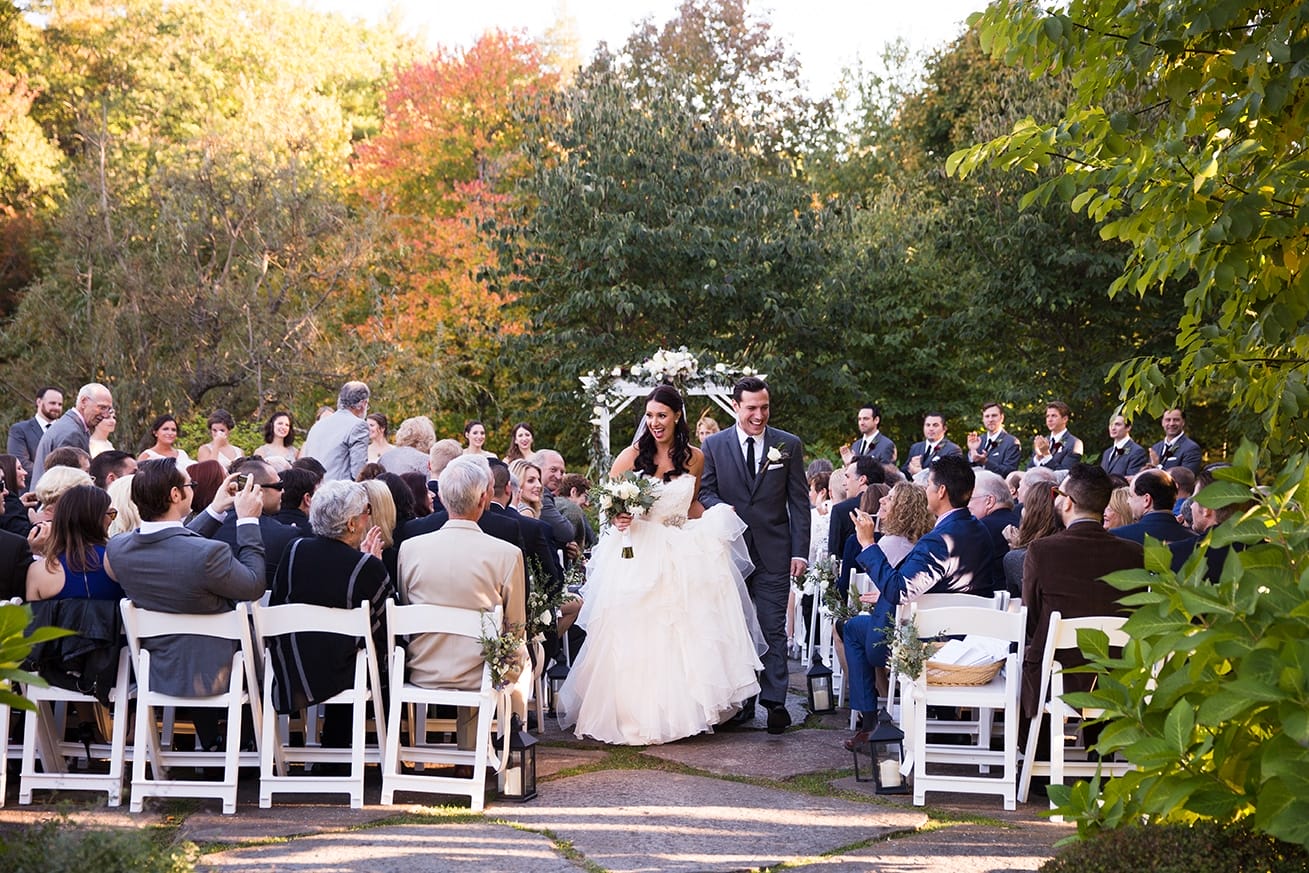 A documentary photograph of a bride and groom walking down the aisle after their outdoor ceremony at Harrington Farm in Princeton, Massachusetts