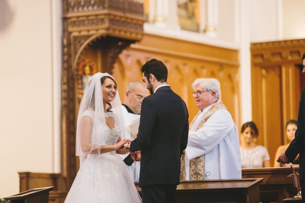 A documentary photograph of a bride and groom exchanging rings during their wedding ceremony at the Cathedral of the Holy Cross