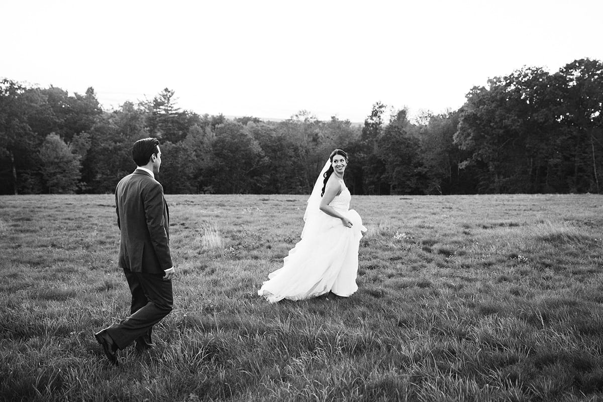 A documentary photograph of a bride and groom walking in a field during their Harrington Farm Wedding in Princeton, Massachusetts