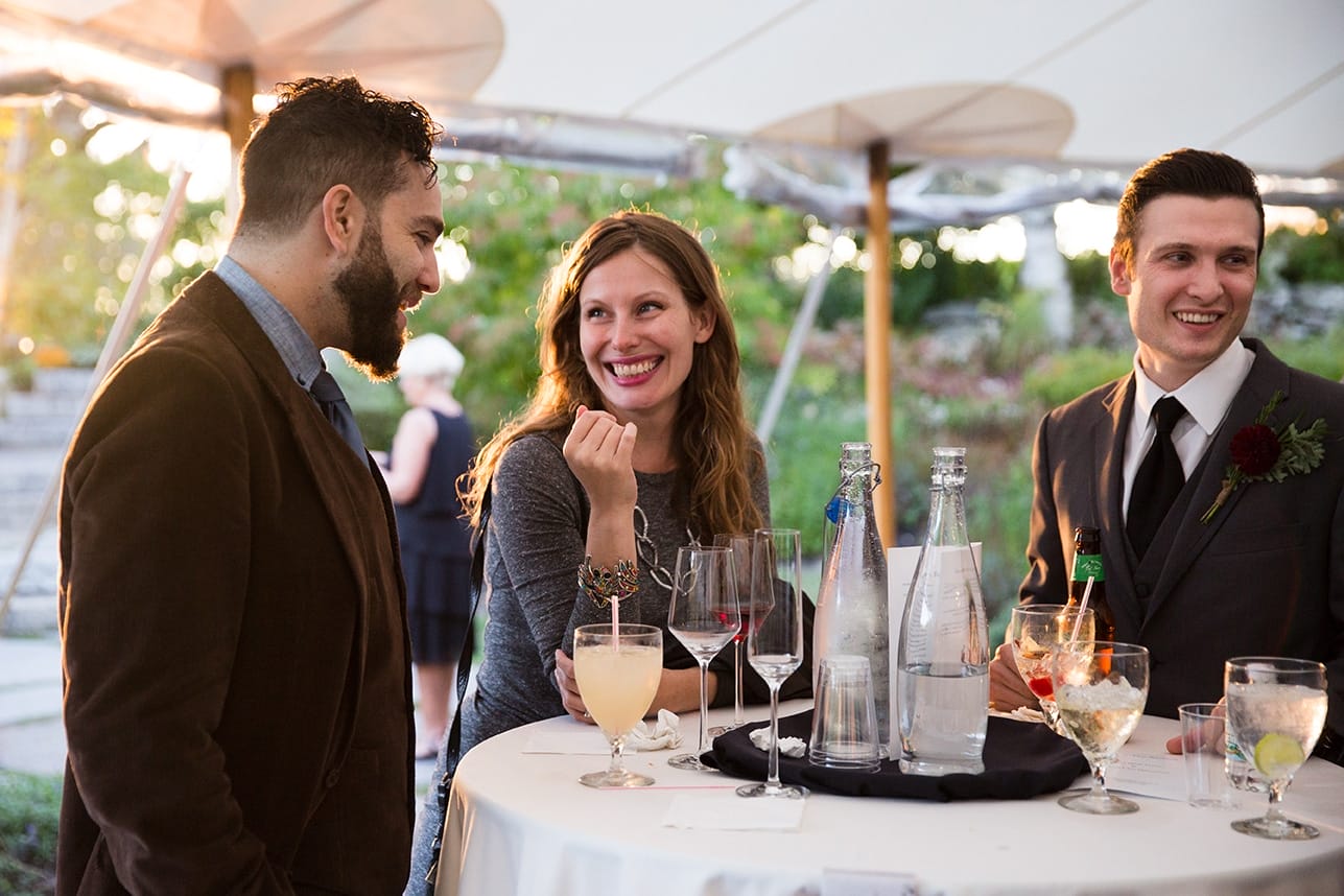 A documentary photograph of guests talking and laughing during the cocktail hour of a Harrington Farm Wedding in Princeton, Massachusetts