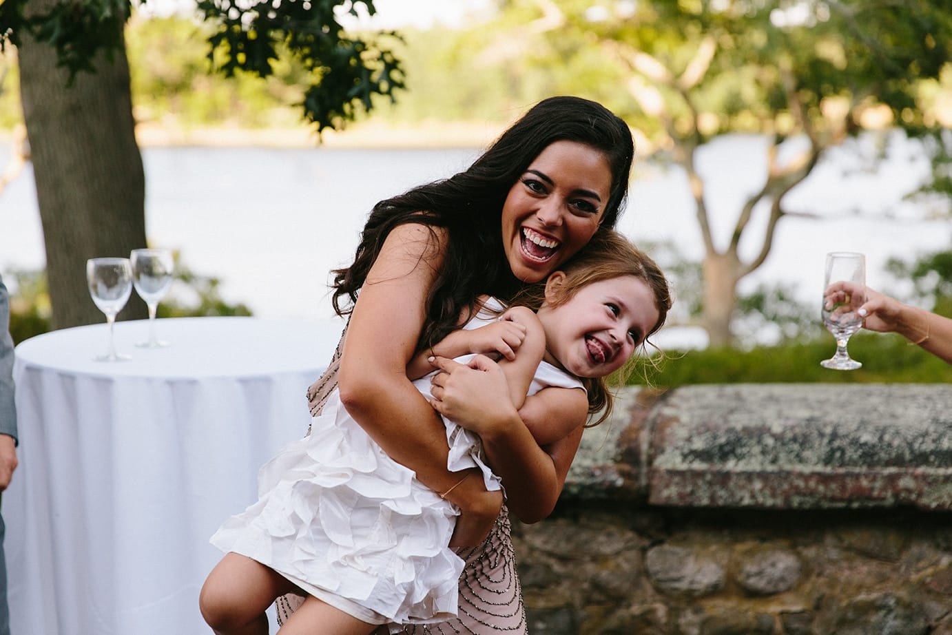 A documentary photograph of a bridesmaid hugging the flower girl at a Moraine Farm Wedding in Beverly, Massachusetts