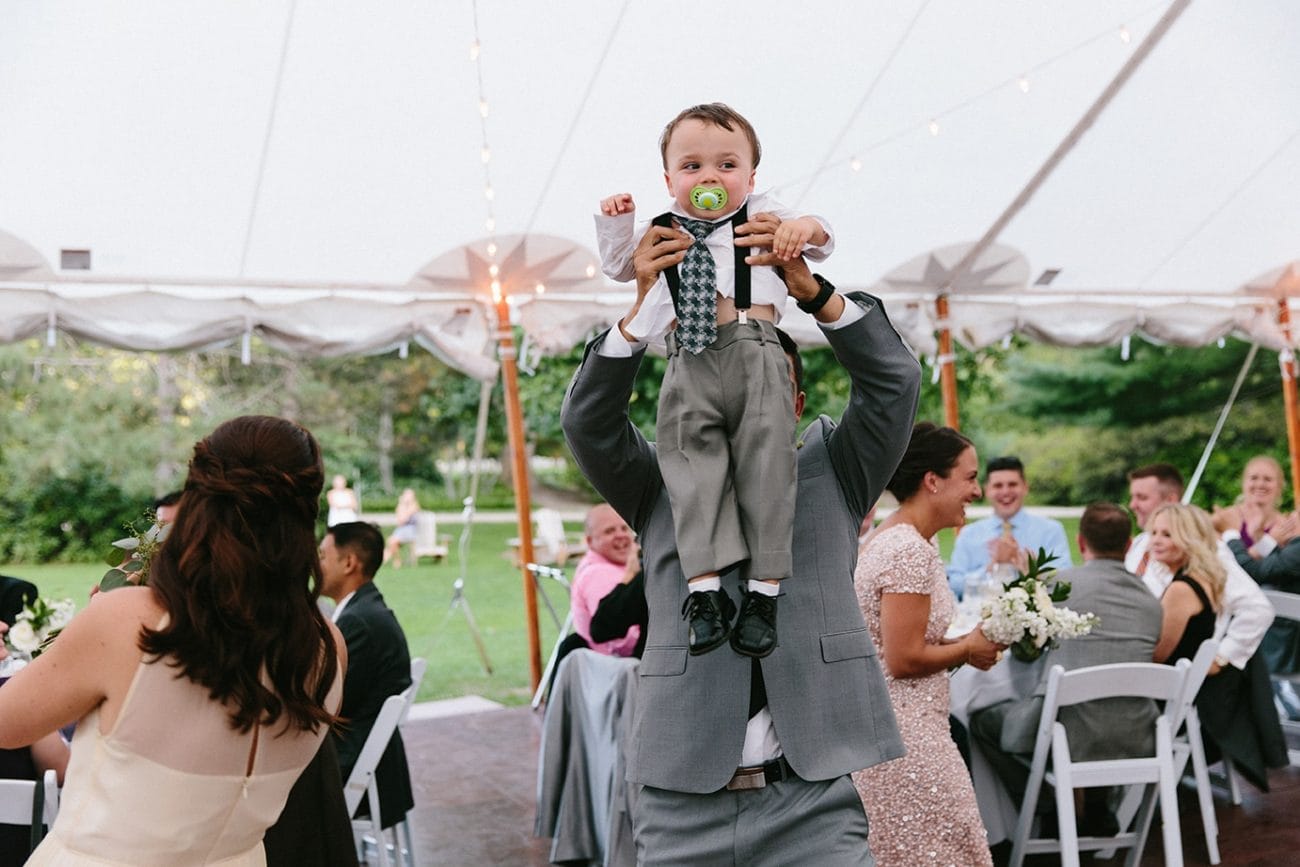 A documentary photograph of the ring bearer entering the reception tent with the best man at a Moraine Farm Wedding in Beverly, Massachusetts
