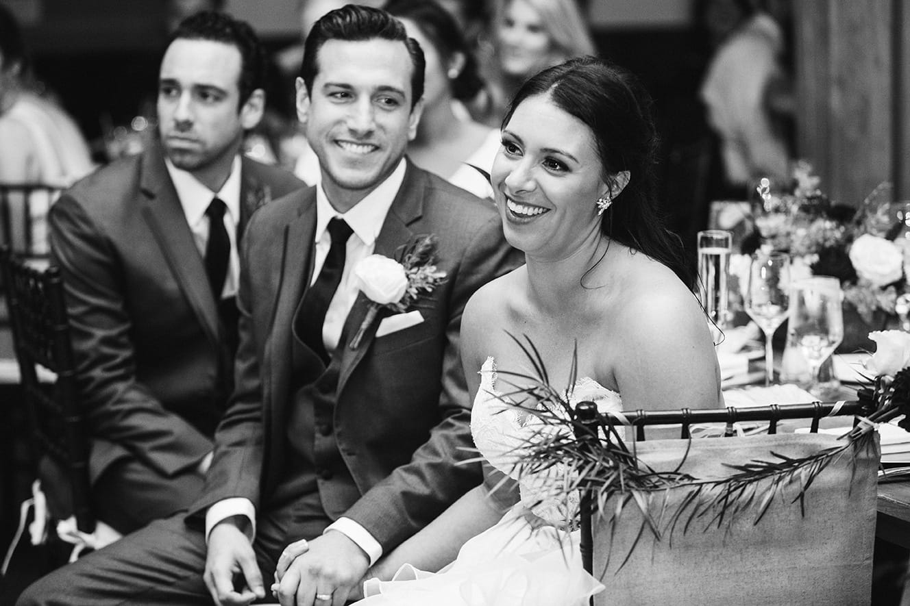 A documentary photograph of a bride and groom smiling during the wedding toasts of their Harrington Farm Wedding in Princeton, Massachusetts