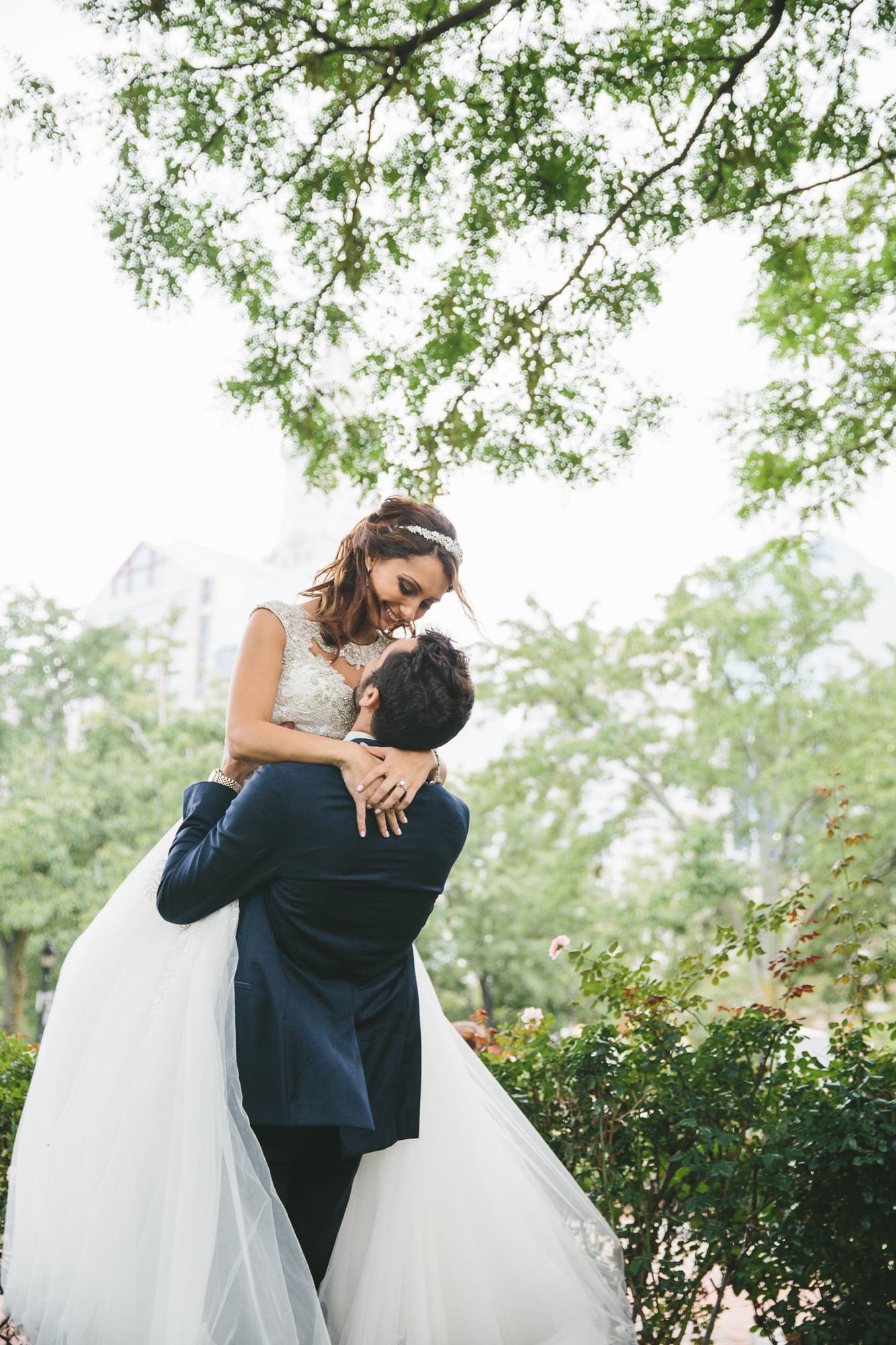 A documentary photograph of a groom lifting up his bride at the Boston Public Gardens during their State Room Wedding