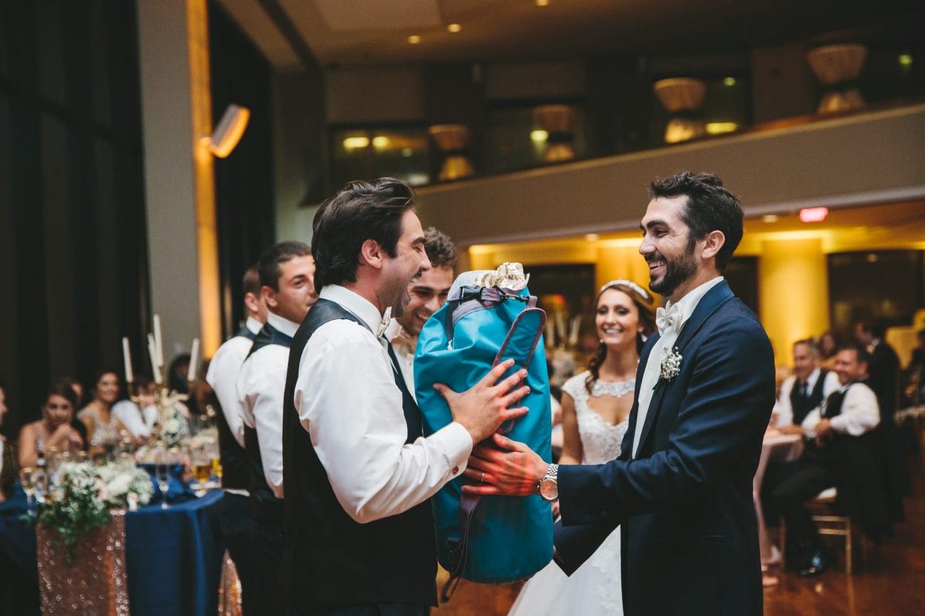 A documentary photograph of a groom giving his groomsmen a present during the toasts at his State Room Wedding in Massachusetts