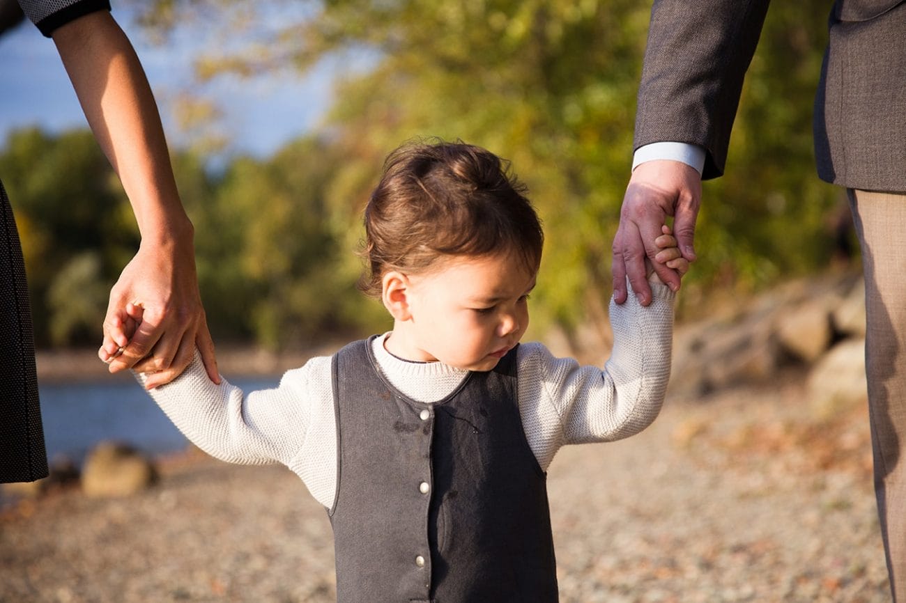 A documentary photograph of a toddler holding his parents hands during a Jamaica Pond family photo session in Boston