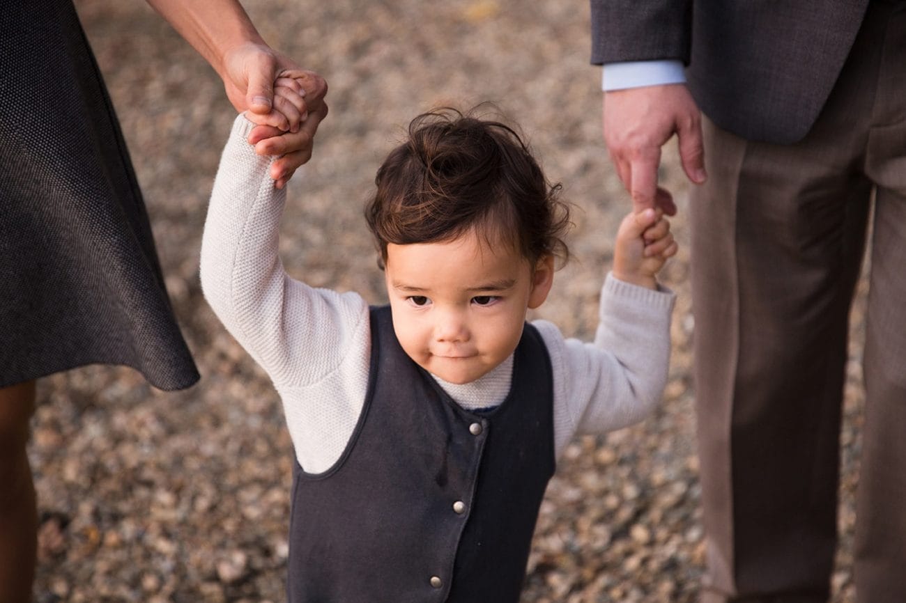 A documentary photograph of a boy holding his parents hand during a Jamaica Pond Family Session in Boston