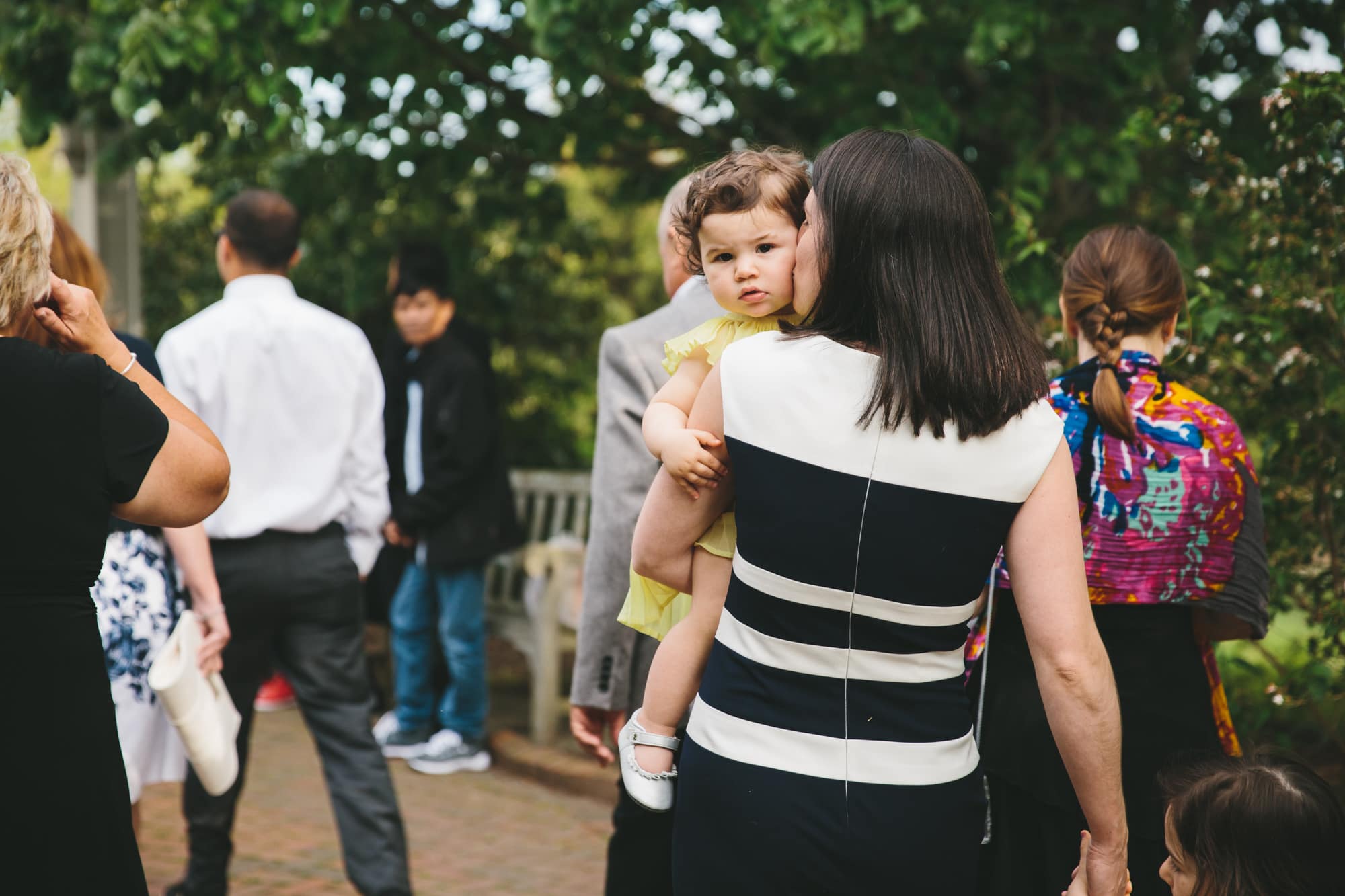 A documentary photograph of a mom kissing her toddler during a Tower Hill Wedding in Boylston, Massachusetts