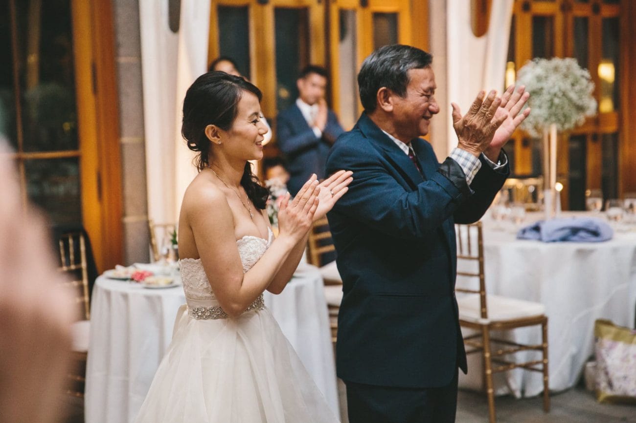 A documentary photograph of a bride and her father clapping during a tower hill wedding reception in Boylston, Massachusetts