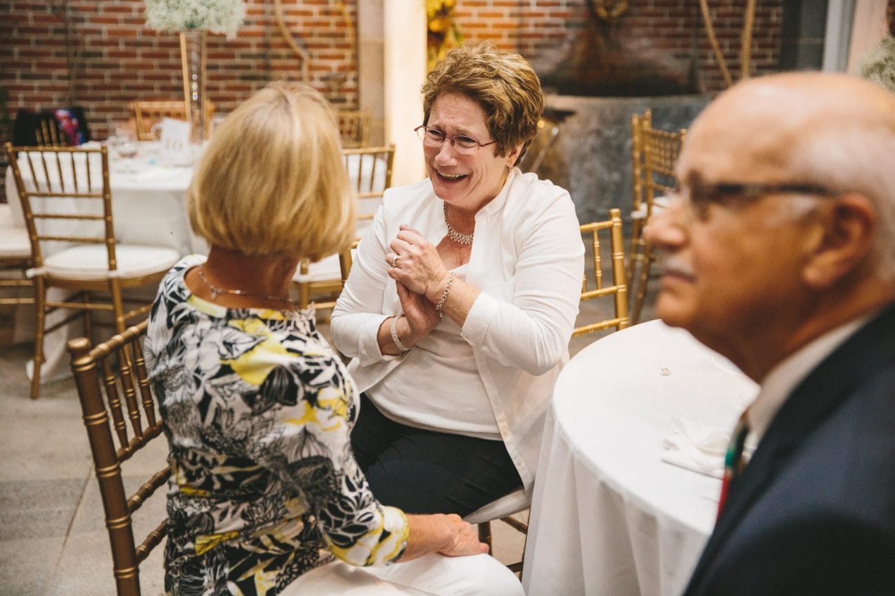 A documentary photograph of guests talking and laughing during a tower hill wedding reception in Boylston, Massachusetts