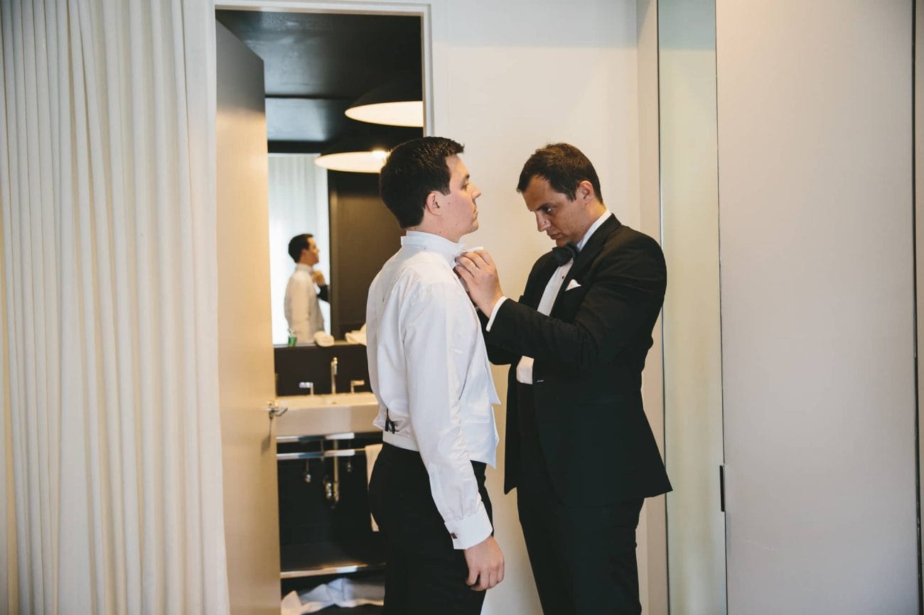 A documentary photograph of the grooms brother tying the grooms bow tie at the Ames Hotel before his State Room Wedding