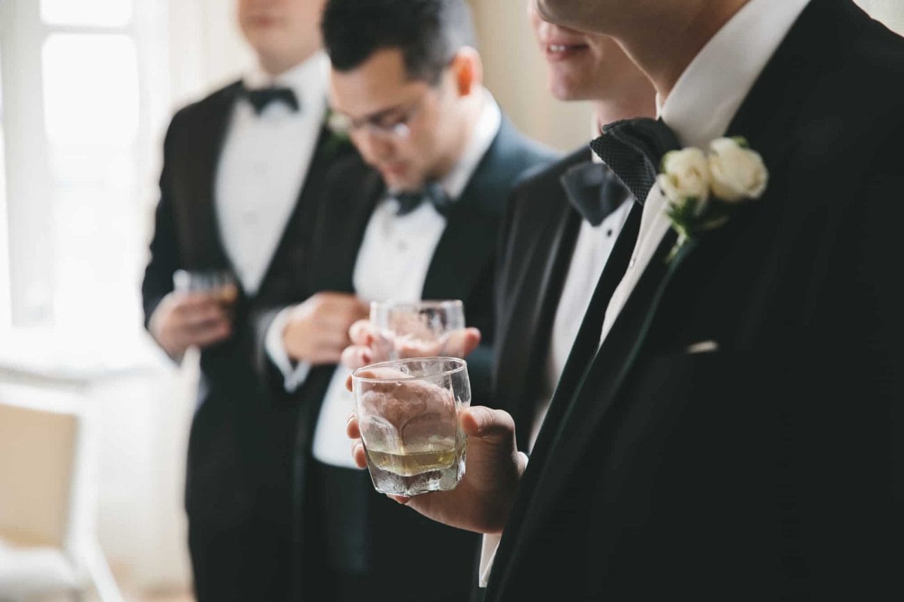 A documentary photograph of groomsmen sharing a drink before a State Room Wedding