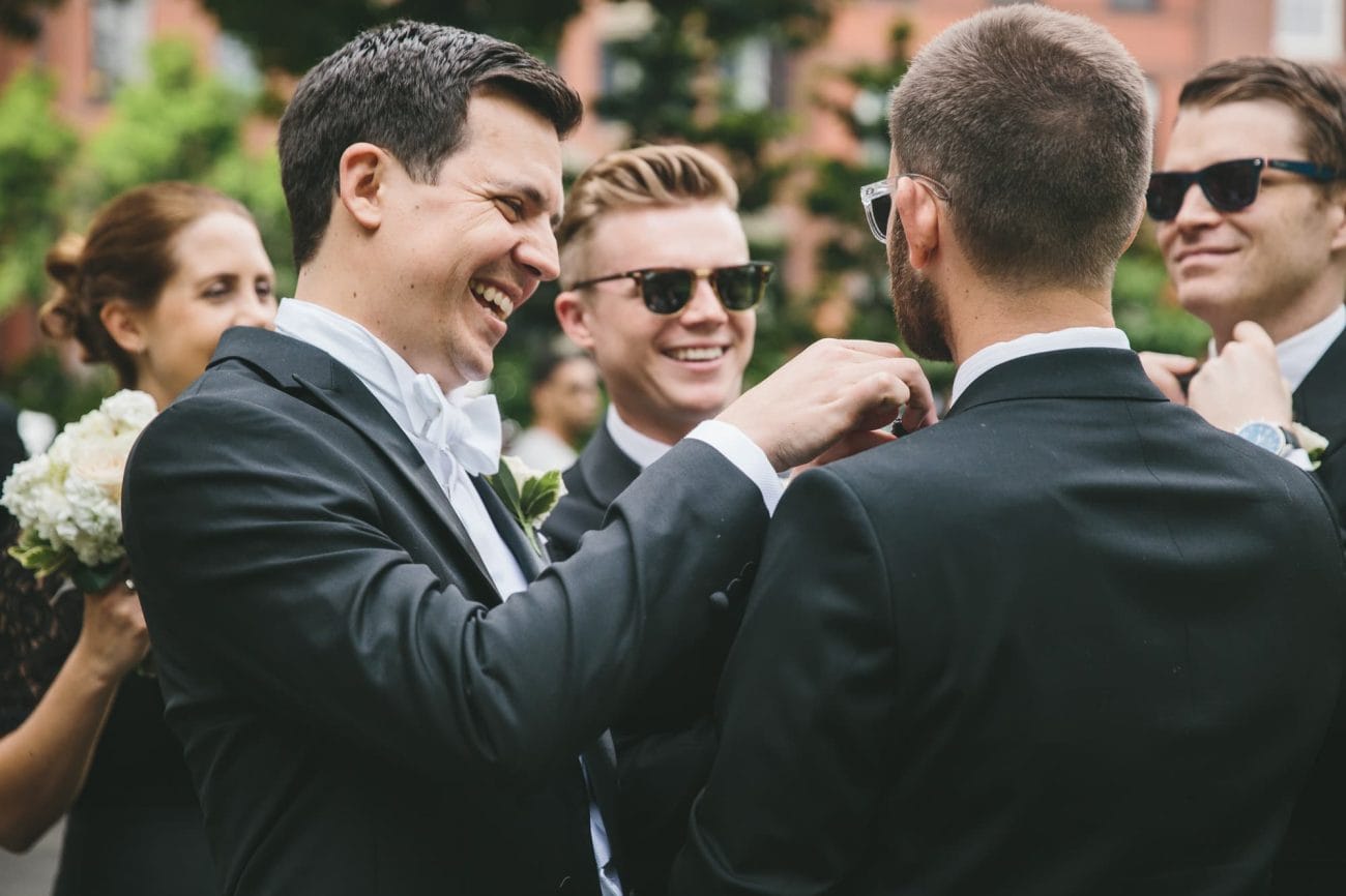 A documentary photograph of a groom helping the groomsmen with their bowties during their portrait session at the Boston Public Gardens before their State Room Wedding