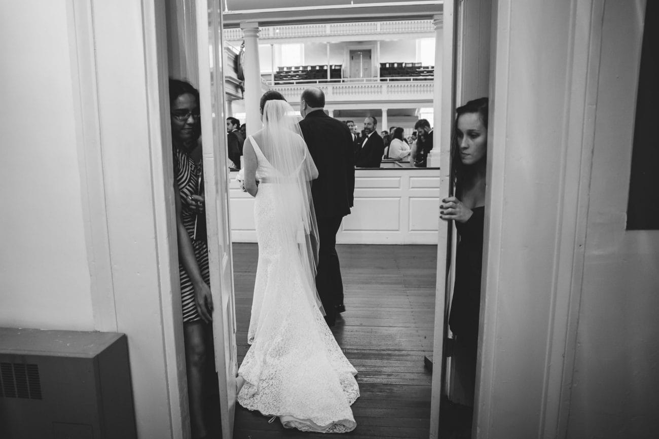 A documentary photograph of a bride walking down the aisle during an old south meeting house wedding ceremony