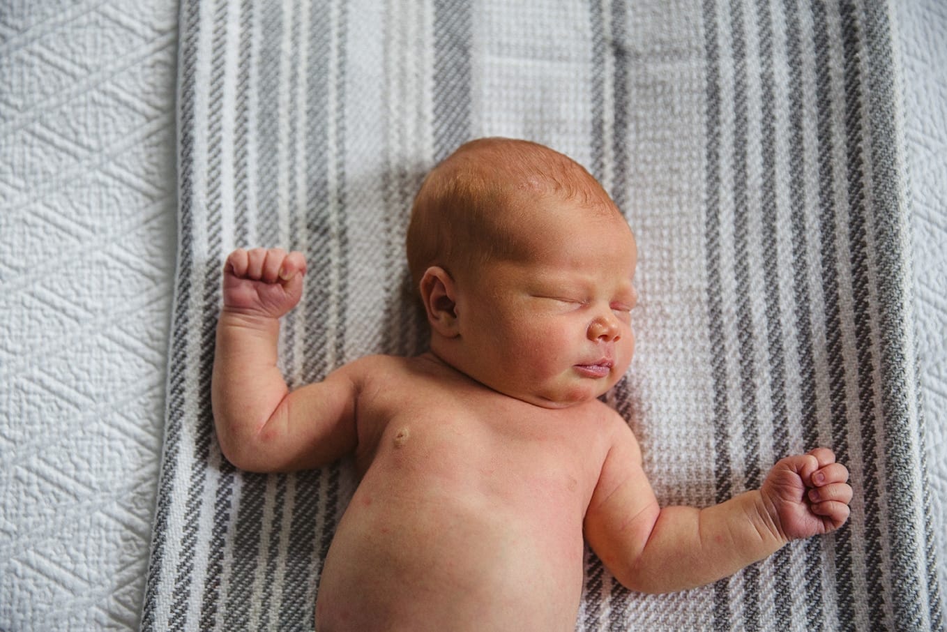 A lifestyle portrait of a newborn laying on the bed during an in home newborn session in Boston, Massachusetts