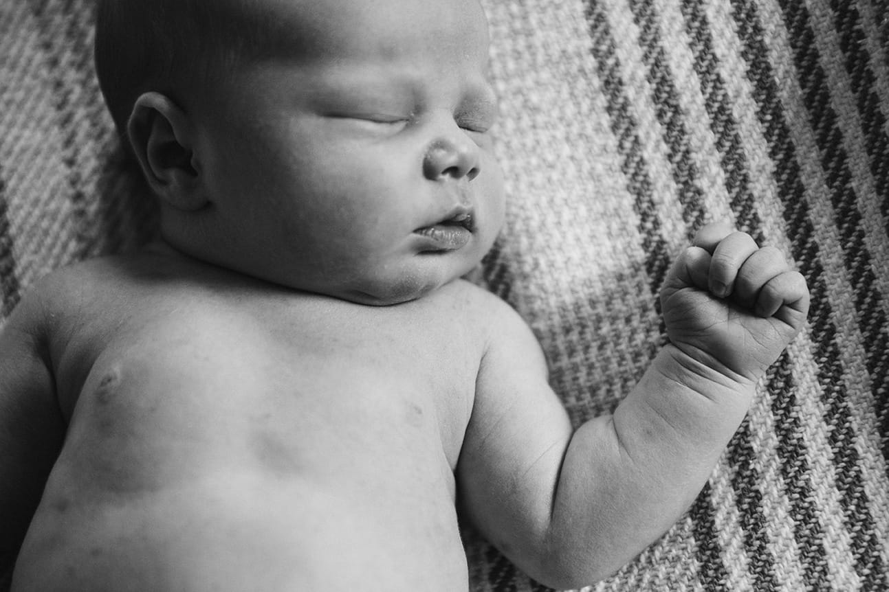 A lifestyle portrait of a newborn sleeping on the bed during a in home newborn session in Boston, Massachusetts