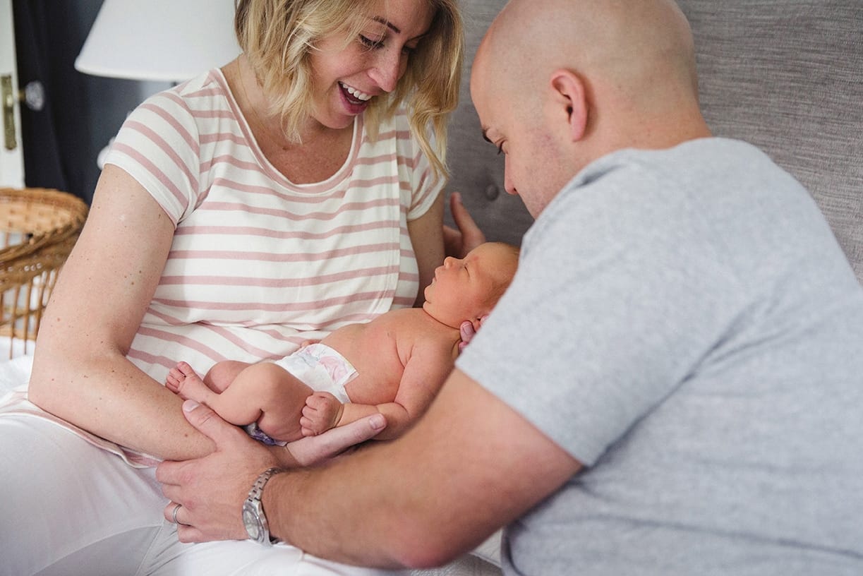 A documentary photograph of new parents holding their newborn daughter in bed during their lifestyle newborn session in Boston, Massachusetts