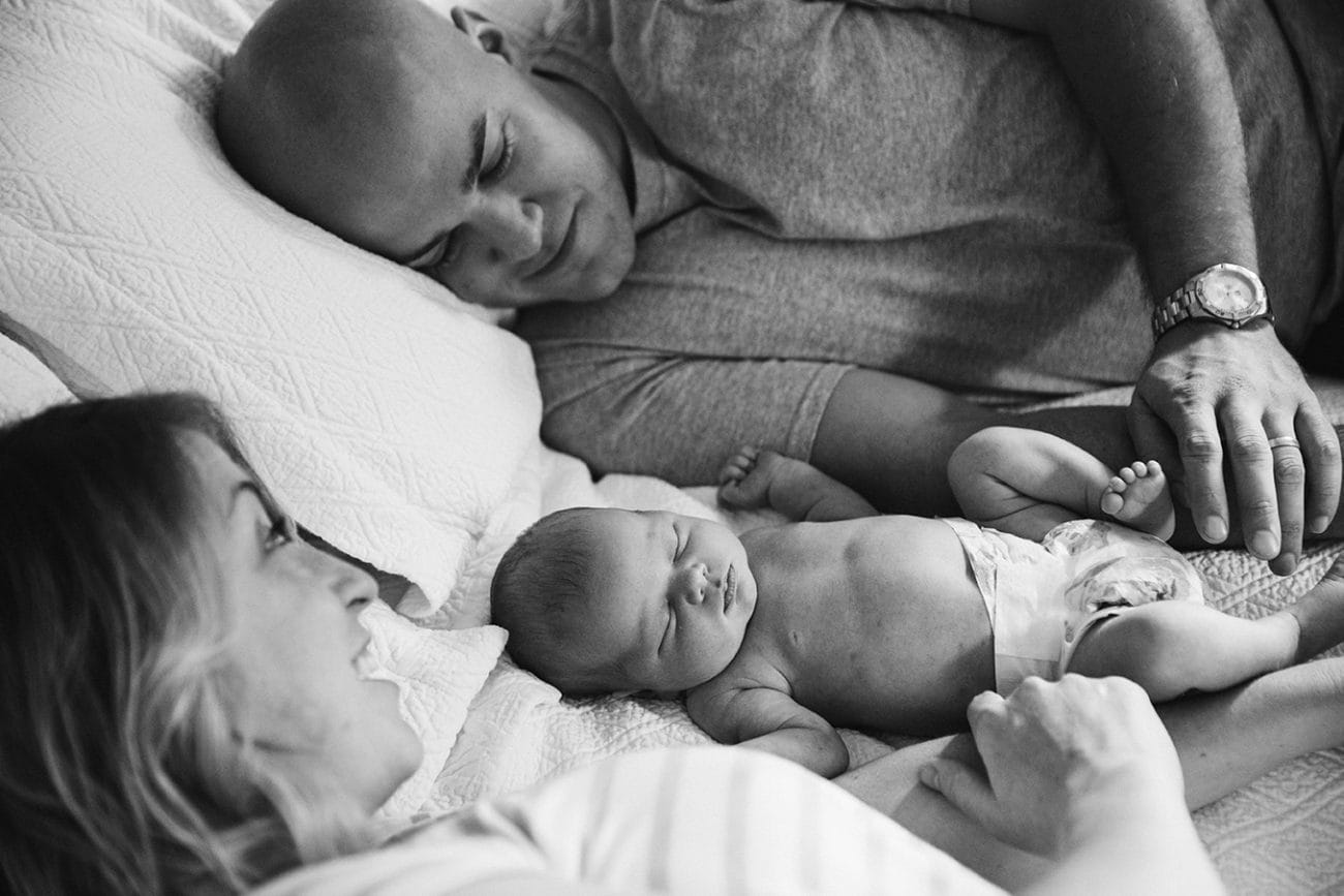 A documentary photograph of new parents laying in bed with their newborn daughter during their lifestyle session at home in Boston, Massachusetts