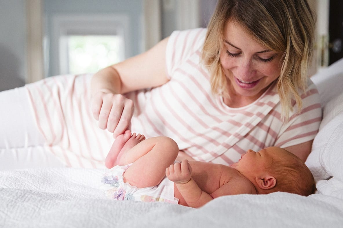 A documentary photograph of a mom laying in bed with her newborn daughter during their in home session in Boston, Massachusetts