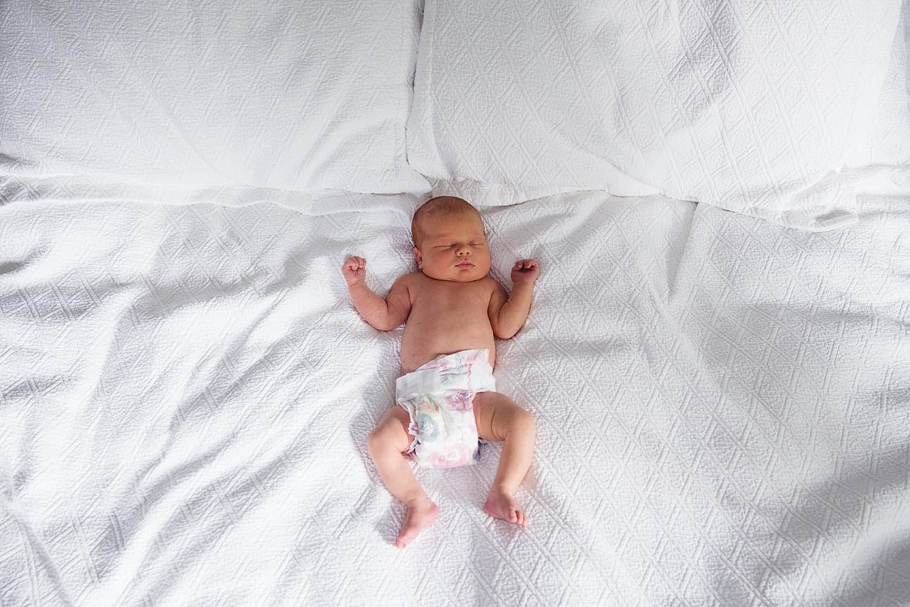 A documentary photograph of a newborn baby laying in her parents bed during a in home session in Boston, Massachusetts