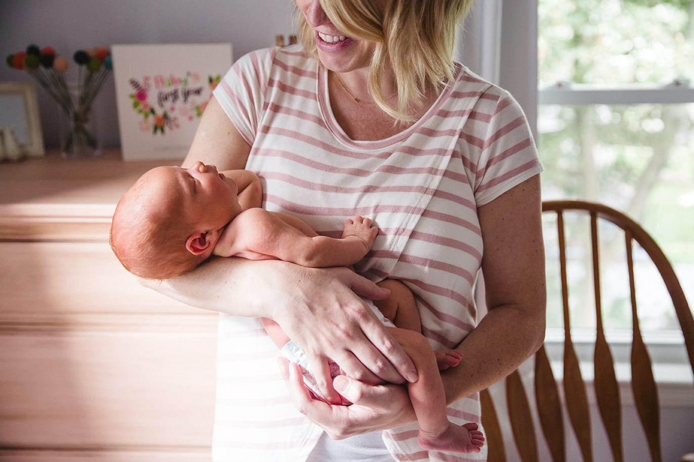 A documentary photograph of a new mom smiling at her newborn daughter during their lifestyle session in Boston, Massachusetts