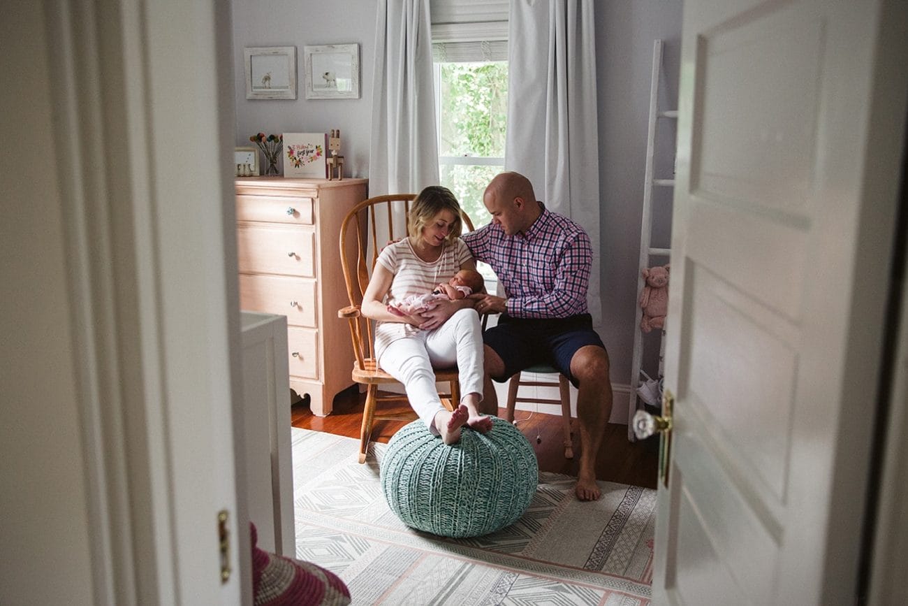A documentary photograph of new parents rocking their newborn daughter in her nursery during an in home lifestyle session in Boston, Massachusetts