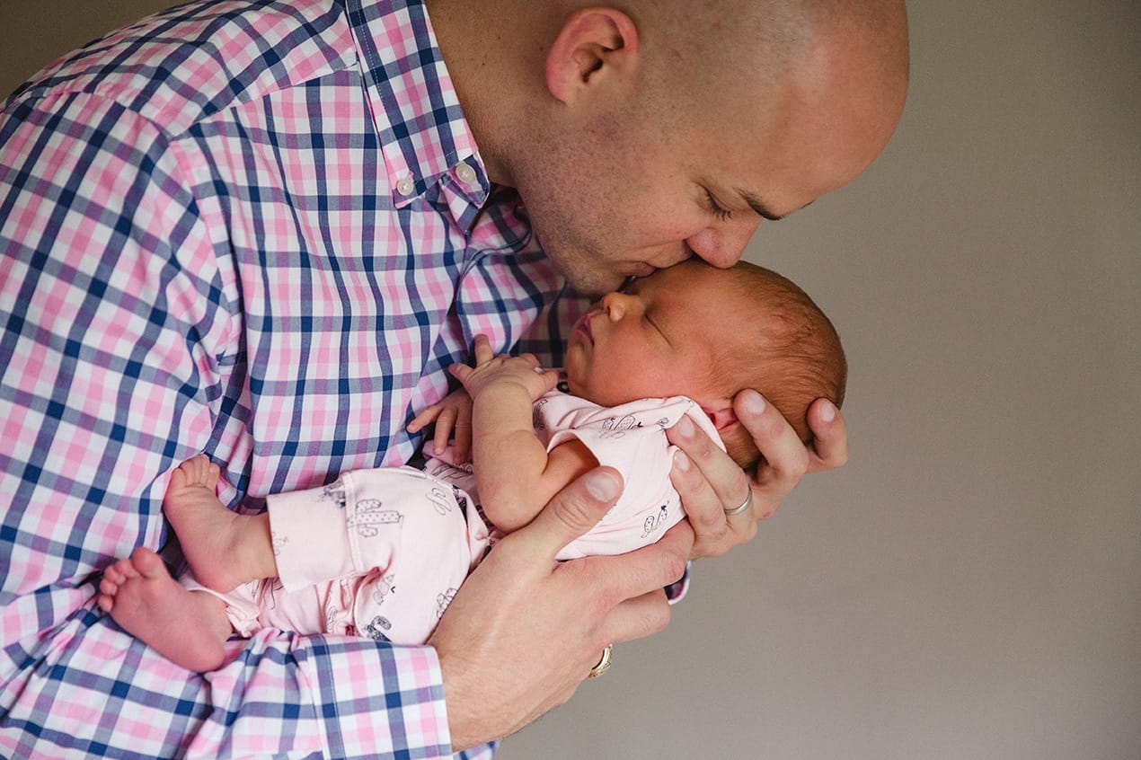 A documentary photograph of a father kissing his new born daughter during their in home lifestyle session in Boston, Massachusetts