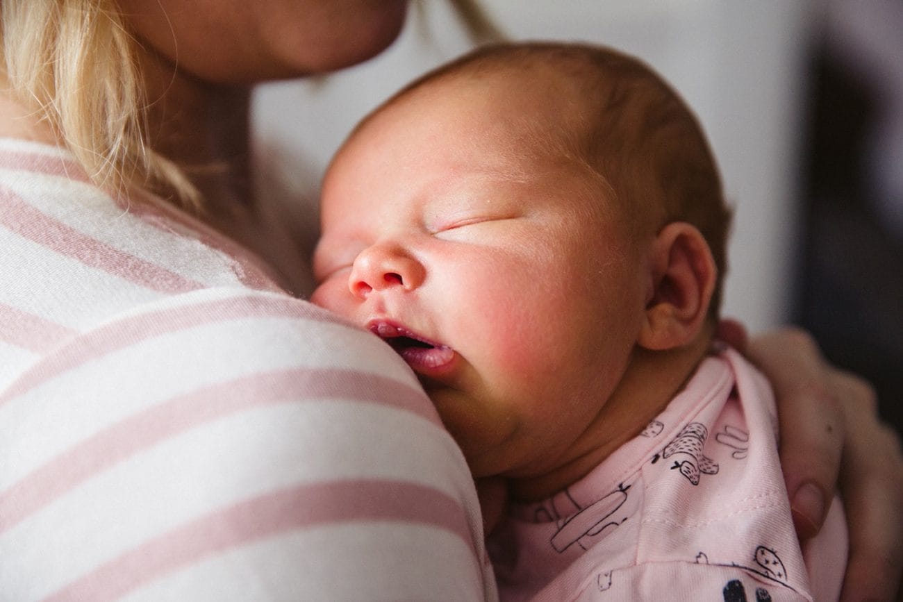 A documentary photograph of a newborn baby sleeping on her mother's shoulder during an in home lifestyle session in Boston, Massachusetts